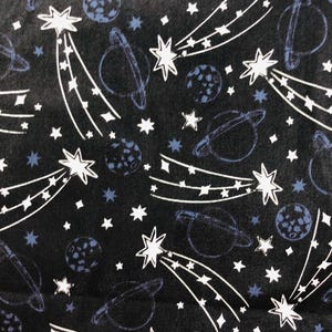 Pode incluir: Tecido preto com um padrão repetido de estrelas cadentes brancas, planetas e estrelas. Os planetas e as estrelas são delineados em branco e azul. Adequado para projetos de artesanato ou vestuário.