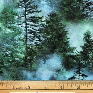 Op de afbeelding: Stof met een boslandschap met hoge groene dennenbomen en een mistige blauwe achtergrond. Langs de onderkant is een liniaal te zien en een label met "Blue Snowman fabrics".