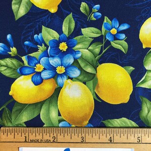 May include: Fabric with a vibrant pattern of yellow lemons, blue flowers, and green leaves on a dark blue background. A wooden ruler with inch measurements is at the bottom. The text "Blue Snowman fabrics" is visible.