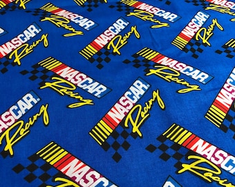 May include: A vibrant blue fabric featuring a repeating pattern of the NASCAR Racing logo. Each logo includes the word NASCAR in white letters on a red and yellow background, accompanied by the word Racing in yellow script and a black checkered flag.