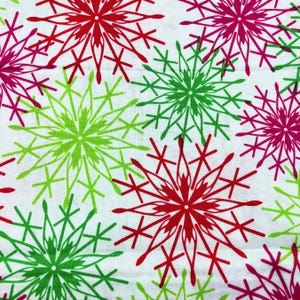 Puede incluir: Tela blanca con un patrón repetido de copos de nieve estilizados en rojo, verde y magenta. Los diseños de los copos de nieve tienen una apariencia de estrella, con múltiples líneas radiantes y formas de cruz.