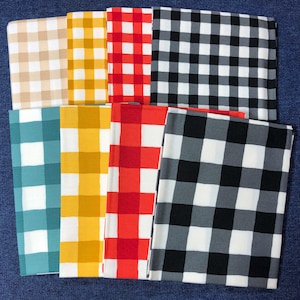 May include: A collection of folded fabric squares in various colors, each featuring a classic gingham pattern. Colors include tan, yellow, red, black and white, teal, and gray. The squares are arranged on a blue surface.