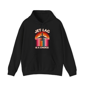 以下が含まれることがあります： 「Jet Lag is a choice」というテキストとレトロな夕焼けのグラフィックがプリントされた黒いフード付きスウェットシャツ。