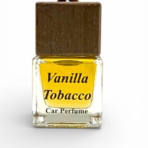 May include: A small, square glass car perfume bottle with a wooden cap and a brown wooden bead. The bottle contains a yellow liquid and features the words "Vanilla Tobacco Car Perfume" in black text.