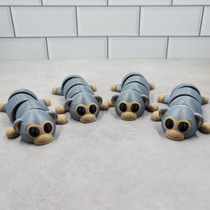 May include: Four gray segmented monkey toys with brown eyes and mouths. The monkeys are arranged in a row on a gray surface.