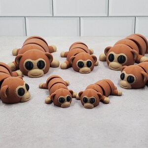 May include: Seven brown monkey figurines with segmented bodies and black eyes. The monkeys are arranged in a row on a white tiled surface.