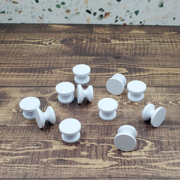 May include: A collection of white plastic knobs, some with a raised center, scattered on a wooden surface.