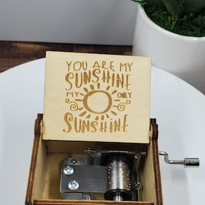 May include: Wooden music box with a sun design and the text "You are my sunshine, my only sunshine". The box is open and the music mechanism is visible.