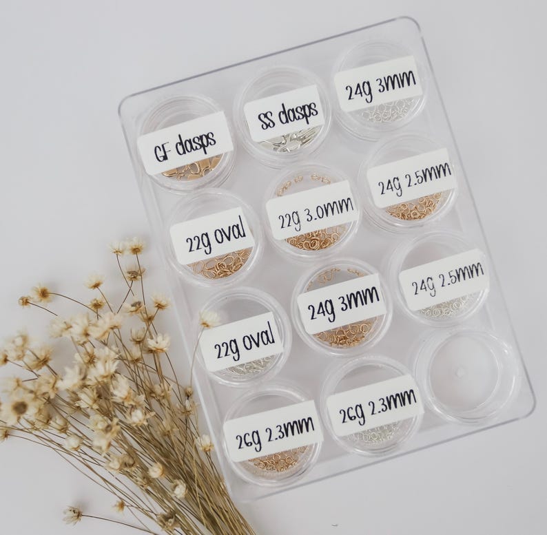 May include: A clear plastic storage container with 10 small containers filled with gold and silver jump rings. Each container has a label with the size and gauge of the jump rings. The labels read: GF dasps, SS dasps, 24g 3mm, 22g oval, 22g 3.0mm, 24g 2.5mm, 22g oval, 24g 3mm, 24g 2.5mm, 2cg 2.3mm, 2cg 2.3mm.