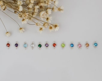 May include: A row of 10 silver charm connectors with different colored gemstones. The gemstones are red, purple, light blue, clear, green, orange, lime green, blue, pink, and gold.