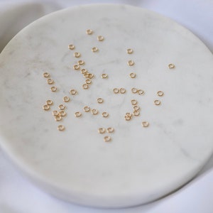 May include: A white marble plate with a scattering of small, gold jump rings.