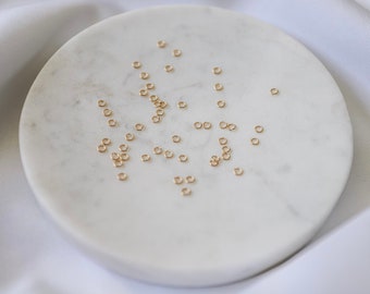 May include: A white marble plate with a scattering of small, gold jump rings.