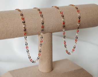 May include: Two gold chains with red, white, and blue enamel beads on a fabric display stand.