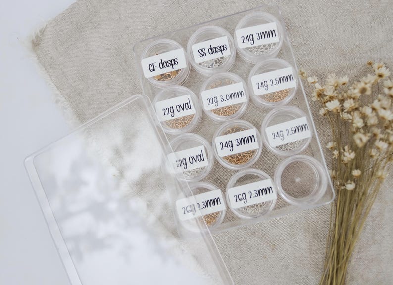 May include: A clear plastic storage box with 10 small containers filled with different types of gold and silver jump rings. The containers are labeled with the size and gauge of the jump rings.  The labels include: GF dasps, SS dasps, 22g oval, 22g 3.0mm, 24g 3mm, 24g 2.5mm, 24g 3mm, 24g 2.5mm, 2cg 2.3mm, 2cg 2.3mm.
