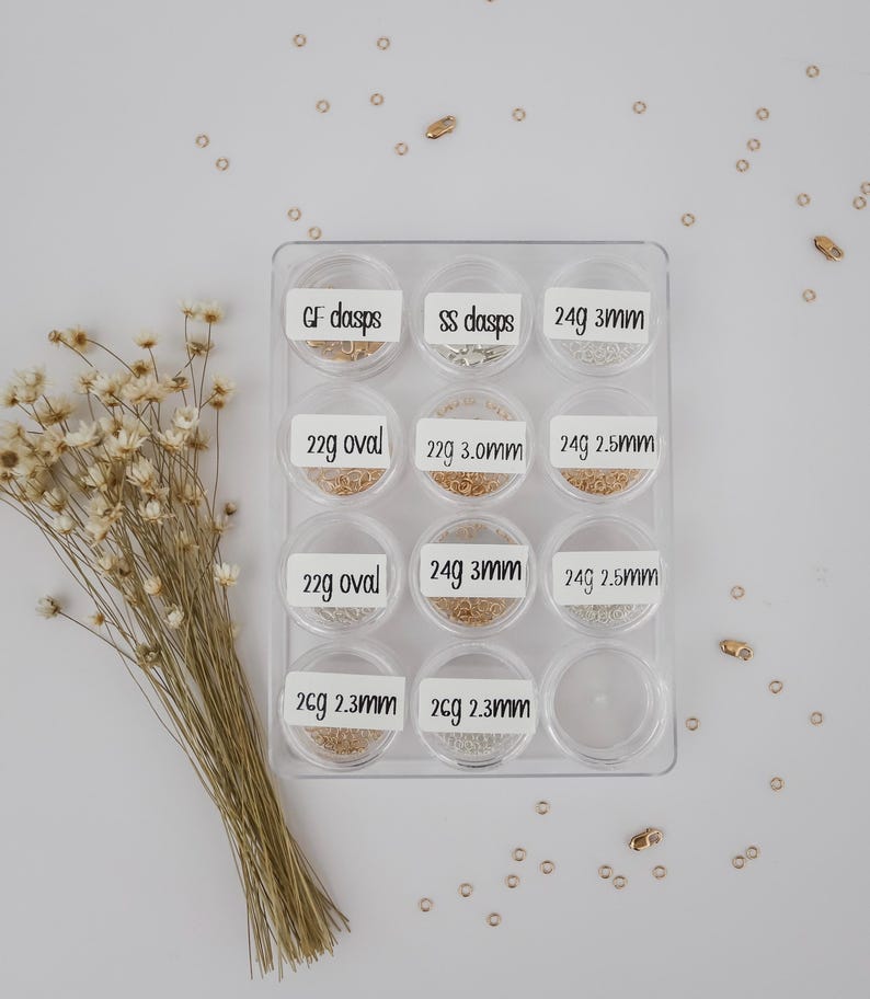 May include: A clear plastic container with 10 compartments, each containing different types of gold and silver jump rings. The compartments are labeled with the size and gauge of the jump rings.  GF dasps, SS dasps, 24g 3mm, 22g oval, 22g 3.0mm, 24g 2.5mm, 22g oval, 24g 3mm, 24g 2.5mm, 26g 2.3mm, 26g 2.3mm.