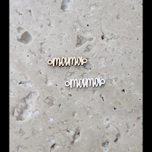 May include: Two metal charms with the word "mama" written in a cursive font. The top charm is gold and the bottom charm is silver.