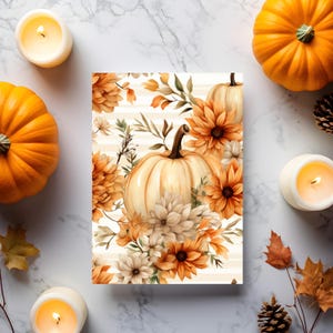 May include: A fall-themed print featuring a white pumpkin surrounded by orange and cream-colored flowers and foliage. The print is set against a striped background. Two orange pumpkins and lit candles frame the print, creating a warm, autumnal scene.