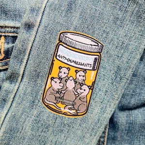 May include: A yellow embroidered patch with a cartoon image of a glass jar labeled "Anti-depressants" containing five cartoon opossums.
