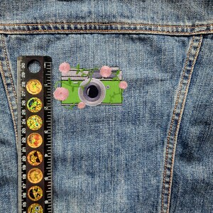 May include: A green camera with a black lens and pink flowers embroidered on a denim jacket.