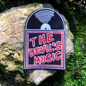 May include: A black and red embroidered patch with a vinyl record design and the text "THE DEVIL'S MUSIC".