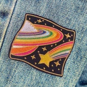 May include: An iron-on patch featuring a rainbow-coloured planet and a shooting star on a black background with gold stars.