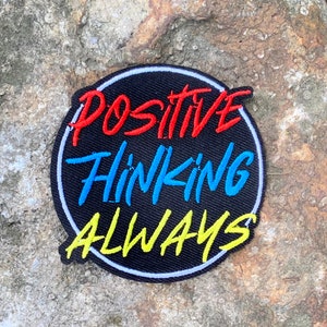 May include: A black circular patch with a white outline. The text "POSITIVE THINKING ALWAYS" is written in a colorful, handwritten style. The words "POSITIVE" and "ALWAYS" are in red and yellow, respectively. The word "THINKING" is in blue.