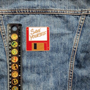 May include: A red and brown floppy disk patch with the text "SAVE YOURSELF" in white lettering.