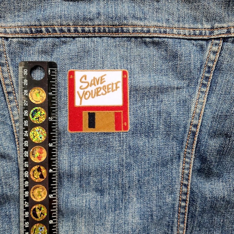 May include: A red and brown floppy disk patch with the text "SAVE YOURSELF" in white lettering.