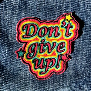 May include: A colorful embroidered patch with the text "Don't give up!" in a retro style. The patch has a red, yellow, and green color scheme with a black outline.