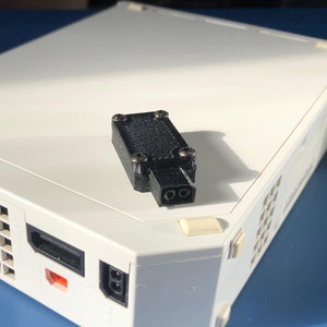 May include: A black plastic power adapter with a two-prong plug, sitting on top of a white Nintendo Wii console.