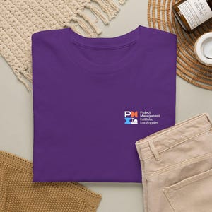May include: A solid purple t-shirt featuring a small logo on the left chest area. The logo displays the letters PMI in white, orange, and blue, accompanied by the text Project Management Institute, Los Angeles in white lettering.