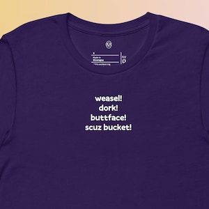 Puede incluir: Una camiseta de color púrpura oscuro con las palabras "weasel! dork! buttface! scuz bucket!" impresas en blanco. La camiseta tiene cuello redondo y mangas cortas. La tela parece suave y cómoda.