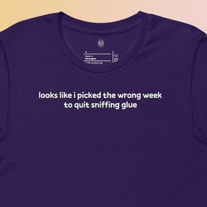 May include: A dark purple t-shirt with the text "looks like I picked the wrong week to quit sniffing glue" in white. The shirt has short sleeves and a crew neck.
