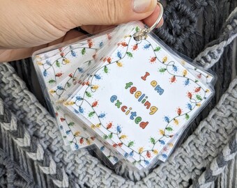 May include: A set of small, square cards held together by a metal ring. Each card has a white background with colorful string lights around the edges. The text "I am feeling excited" is printed on the cards in various colors.