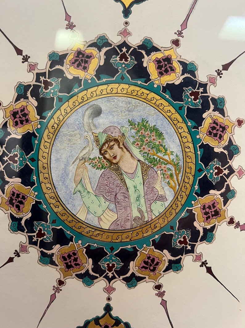 May include: A circular painting featuring a figure in a lavender and green outfit with a feathered headpiece, holding a white bird. The central image is surrounded by an intricate, multi-colored border of dark blue, gold, and teal floral patterns.