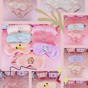 Puede incluir: Una colección de antifaces de felpa para dormir con varios personajes de dibujos animados. Cada antifaz tiene un exterior suave y difuso en colores como blanco, rosa, azul y morado, con un reverso de satén liso y una banda elástica.