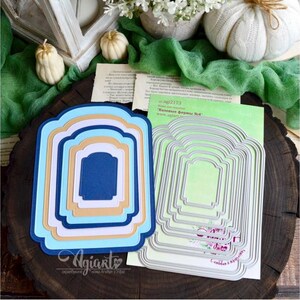 Puede incluir: Un conjunto de formas troqueladas anidadas en varios colores, incluyendo azul, blanco y beige, dispuestas sobre una superficie de madera. También se ve un conjunto de formas troqueladas de metal. La imagen incluye elementos decorativos como calabazas y flores.