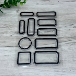May include: A clear sheet of transparent stamps with 10 different black frame designs. The frames are various shapes and sizes, including circles, squares, and rectangles.