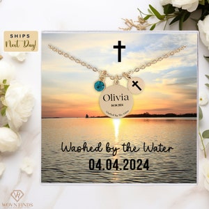May include: A gold necklace with a cross charm, a round charm with the name Olivia and the date 04.04.2024, and a turquoise gemstone. The necklace is displayed in a white box with a sunset and water background. The text "Washed by the Water" and the date 04.04.2024 are printed on the box.
