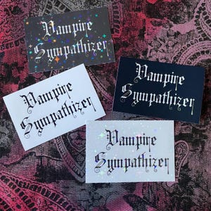 Könnte beinhalten: Vier rechteckige Karten mit dem Text "Vampire Sympathizer" in gotischer Schrift. Die Karten sind schwarz, weiß und irisierend, mit Sternen und Glitzerakzenten. Die Karten sind auf einem gemusterten Hintergrund angeordnet.