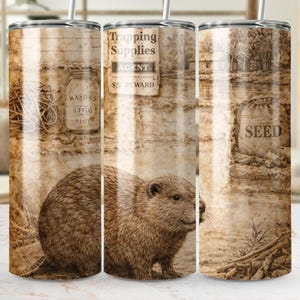 Op de afbeelding: Een roestvrijstalen beker met een vintage ontwerp. Het heeft een beverillustratie, de tekst "Trapping Supplies" en "Seed". Het sepia-getinte ontwerp geeft het een rustieke uitstraling. Geschikt voor warme en koude dranken.
