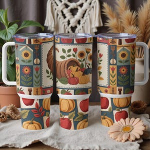 May include: Three insulated travel mugs with white handles and lids. The mugs feature a fall harvest design with pumpkins, apples, sunflowers, and a cornucopia. The design is set against a patchwork background with a blue, beige, and red color scheme.