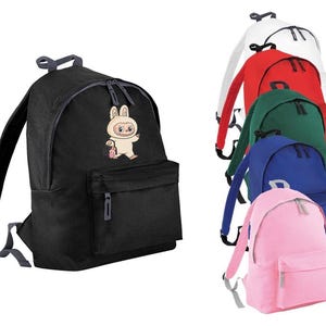 May include: Black backpack with a front pocket and a cartoon bunny design. Additional backpacks in white, red, green, blue, and pink are also visible. The backpacks have adjustable straps and a top handle.