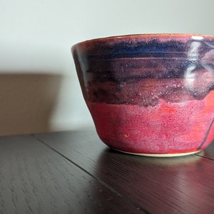 May include: A red and blue ceramic bowl with a glossy finish. The bowl has a wide rim and a rounded bottom.