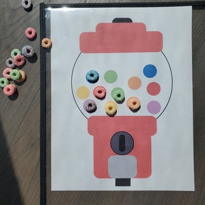 Puede incluir: Una máquina de chicles roja con una ventana de plástico transparente. La máquina de chicles tiene una ranura para monedas y una manija para dispensar los chicles. Hay chicles de colores dentro de la máquina.