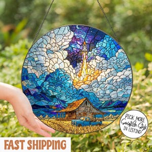 May include: Round stained glass suncatcher with a space theme. The design features a rocket launching into a starry sky above a rustic barn and a blue pickup truck. The color palette includes blues, oranges, and browns.
