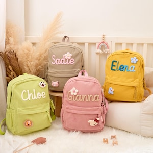 Pu&ograve; includere: Quattro zaini in velluto a coste dai colori pastello: verde, rosa, beige e giallo. Ogni zaino ha un nome ricamato: Chloe, Gianna, Sadie ed Elena. Gli zaini hanno toppe a tema floreale e animale.