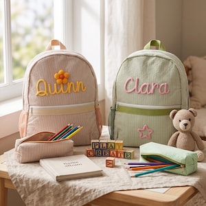 Könnte beinhalten: Zwei gestreifte Rucksäcke, einer beige mit dem Namen Quinn und einer gelben Blume, einer grün mit dem Namen Clara und einem rosa Stern. Enthält zwei passende Federmäppchen mit Buntstiften, ein Notizbuch mit der Aufschrift name album und Holzklötze.