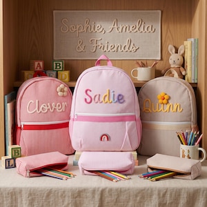 Può includere: Tre zaini a righe e astucci abbinati in rosso, rosa chiaro e beige. Gli zaini presentano i nomi ricamati Clover, Sadie e Quinn con dettagli a forma di fiore o arcobaleno. Ogni zaino è dotato di una tasca frontale con cerniera e manico.