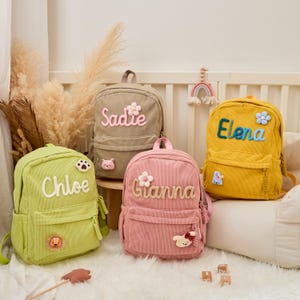Pu&ograve; includere: Quattro zaini in velluto a coste in verde, beige, rosa e giallo. Ogni zaino ha un nome ricamato: Chloe, Sadie, Gianna ed Elena. Gli zaini hanno toppe decorative e dettagli floreali.
